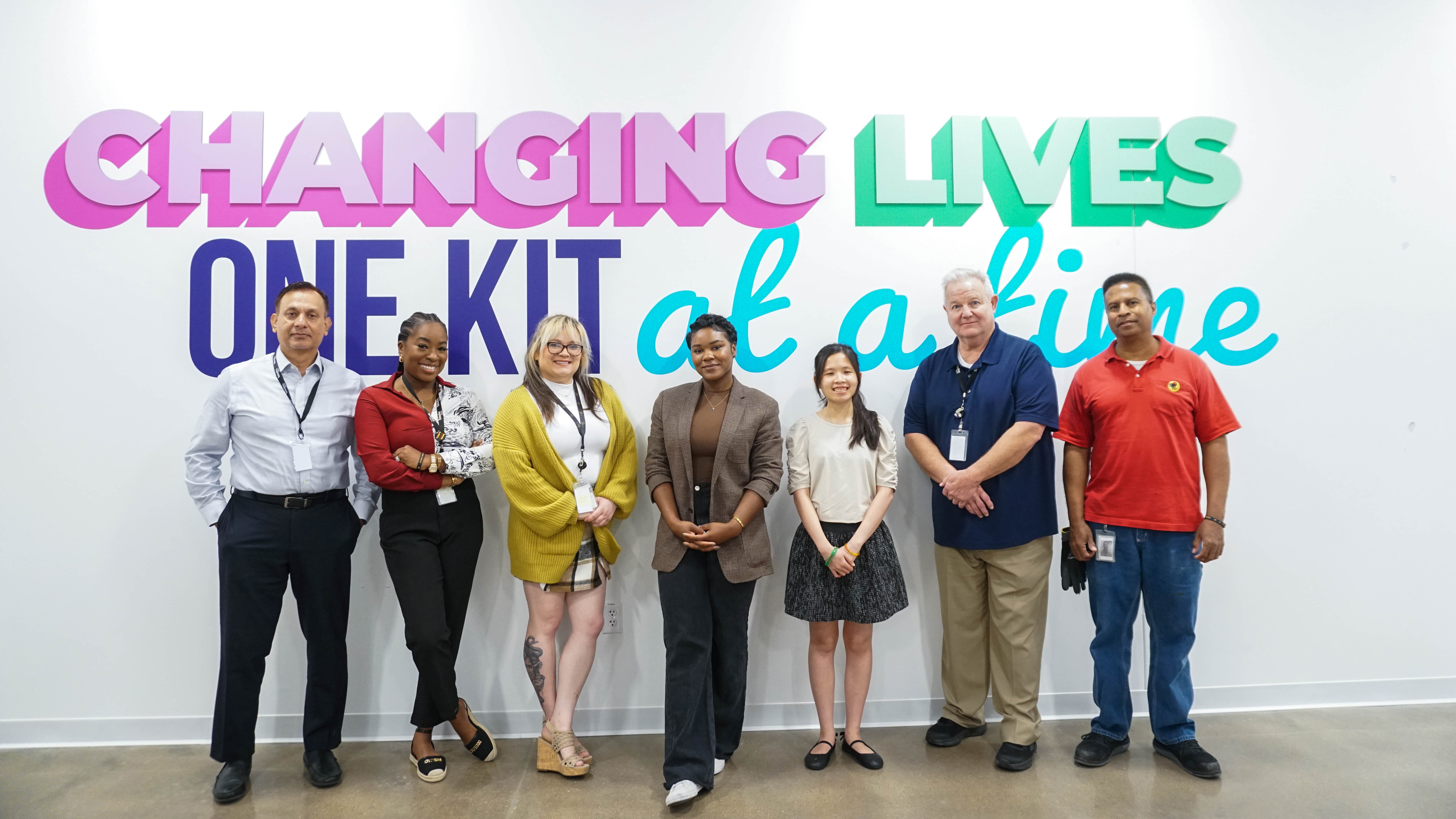 Team in front of sign 'Changing lives one kit at a time'