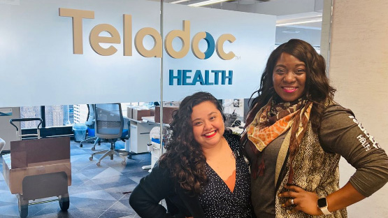 Two women standing in front of Teladoc Health sign on wall