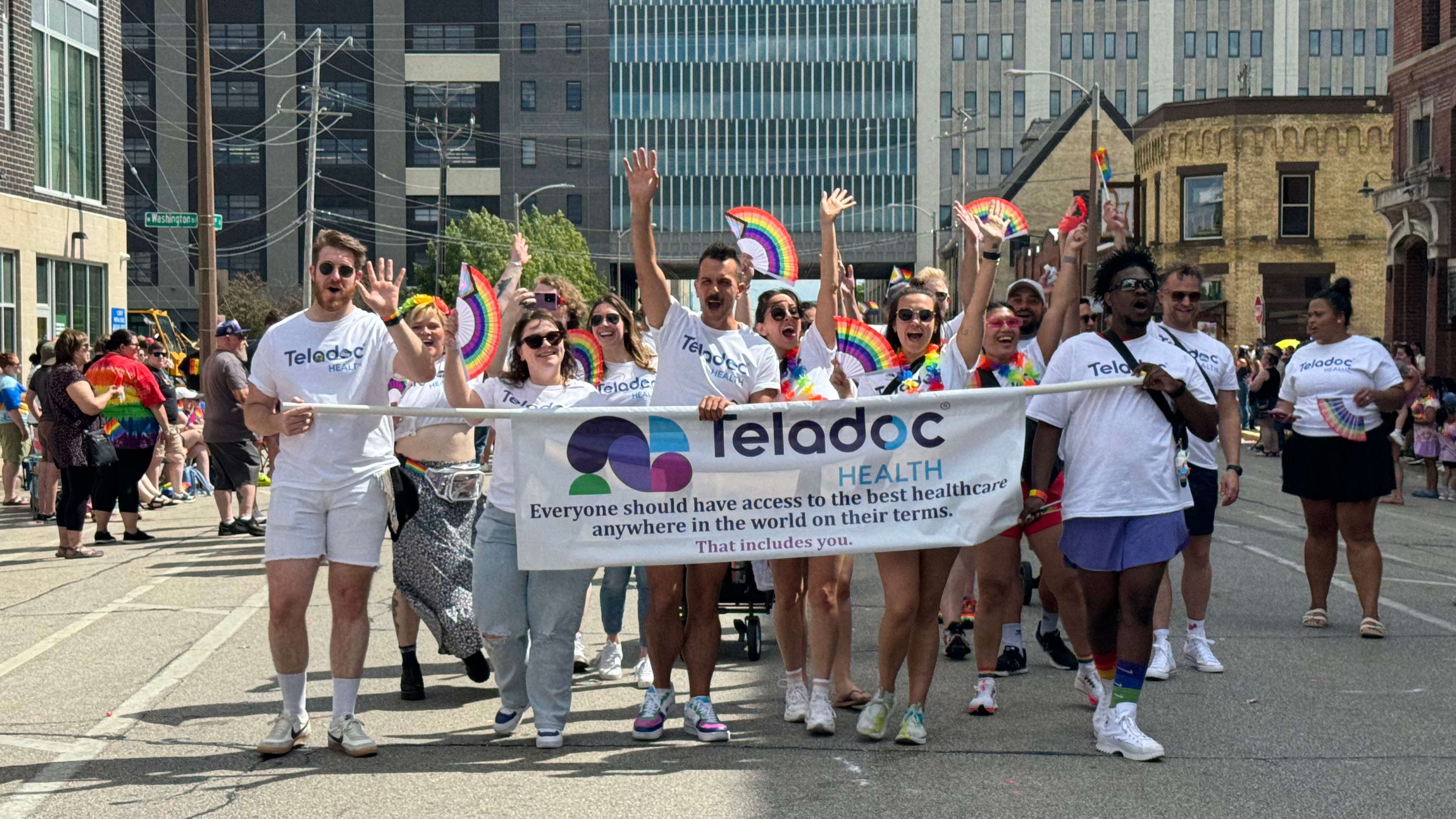 People walking in parade behind Teladoc Health banner