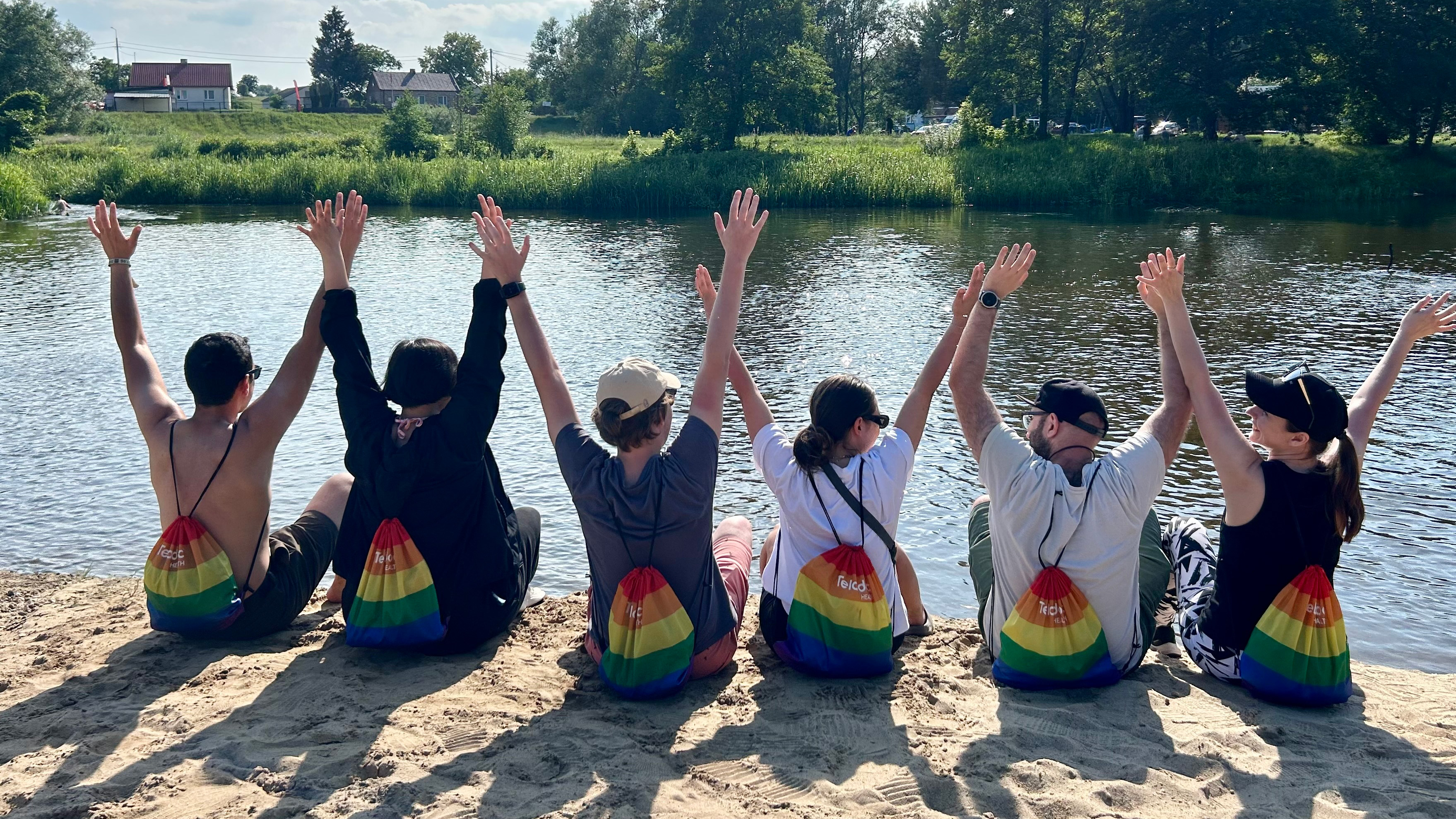 People sitting with back to camera and hands up with rainbow colored backpacks on