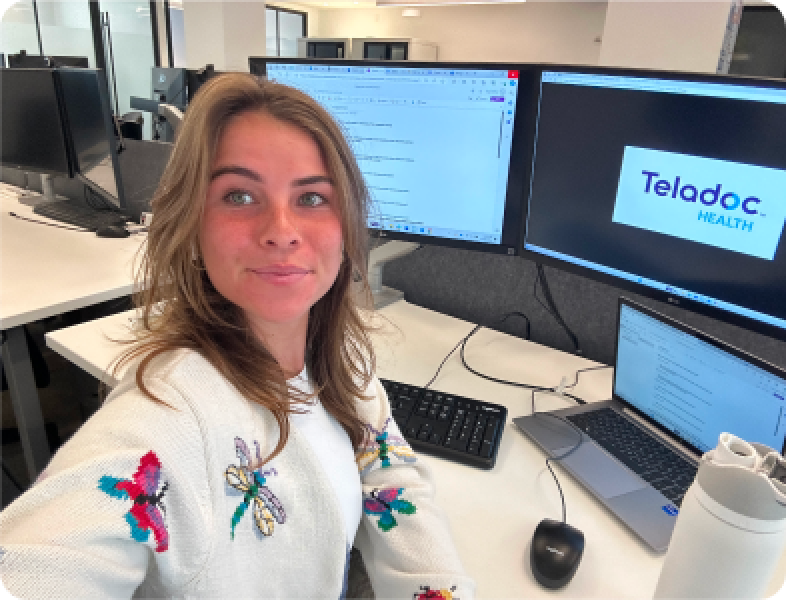 An intern in the office with a TV in the background showing the teladoc Health logo.