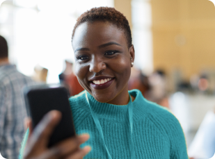 A young professional woman in a blue sweater smiles while looking at her phone, exuding a sense of happiness and engagement.