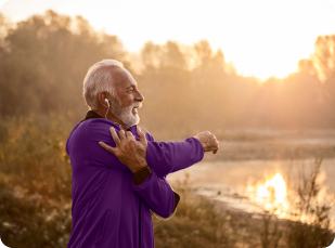 An elderly man wearing a purple shirt walks outside, stretching his arms in a joyful, confident manner.