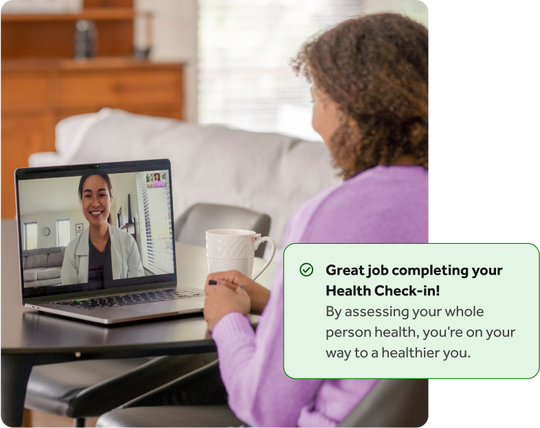 Woman with curly hair in a purple shirt talking to a doctor on her laptop at a table, with an overlay of a Teladoc Health health check-in completion notification.