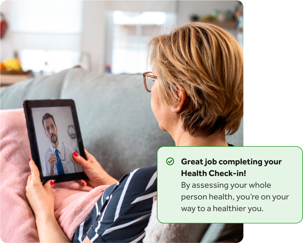 Woman sitting on a couch with her tablet having a video call with a doctor, with an overlay of a Teladoc Health health check-in completion notification.