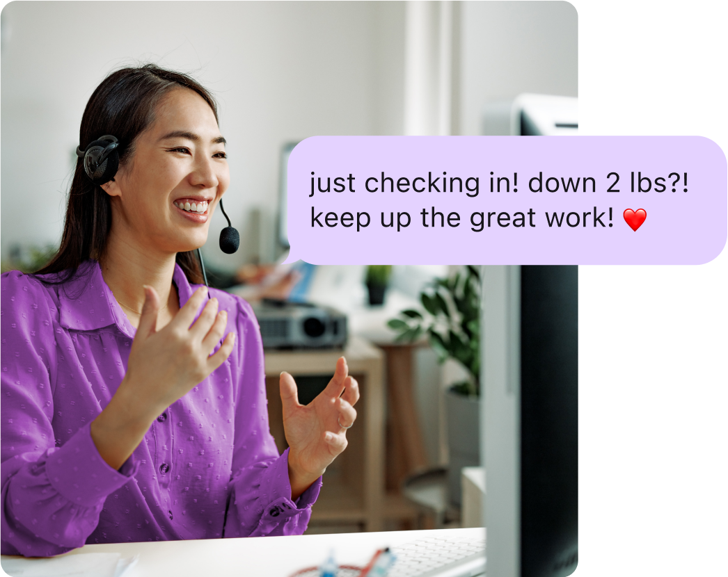 Woman with a headset smiling and talking to her computer, with an overlay of a coaching message reading 'Just checking in! Down 2 lbs?! Keep up the great work!'