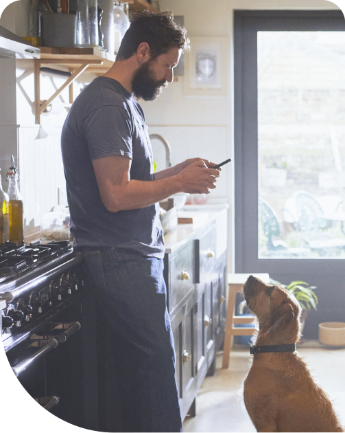 Man checks his Teladoc app on his phone while his dog stands by him