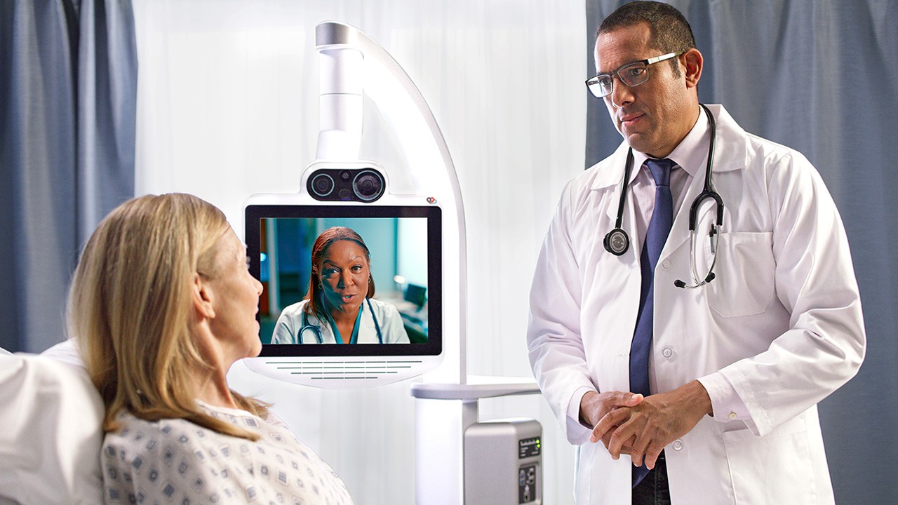 Doctor talking with patient in hospital room and doctor on virtual device