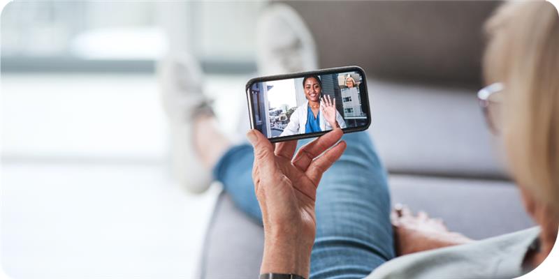Person sitting on a couch holding a phone and video chatting with a doctor